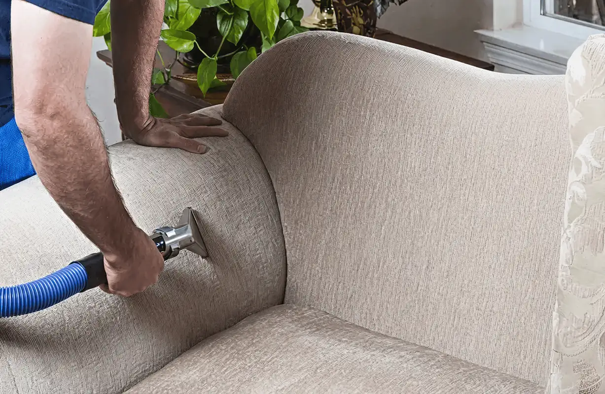 Professional upholstery cleaner deep-cleaning a fabric sofa with a handheld extraction tool and hose, Cape Coral, FL.